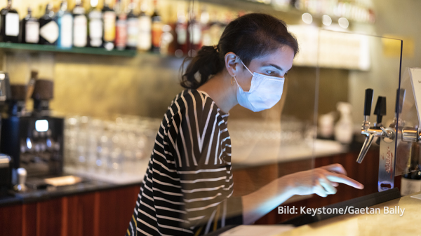 Angestellte mit Maske bedient an der Bar die Kasse.